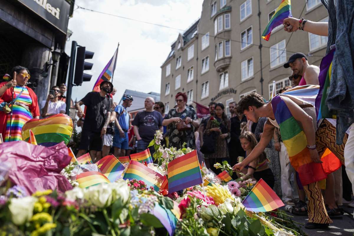 People with Pride flags stand near the London pub and lay flowers on June 25, 2022, in the aftermath of a shooting outside pubs and nightclubs in central Oslo killing two people injuring 21.