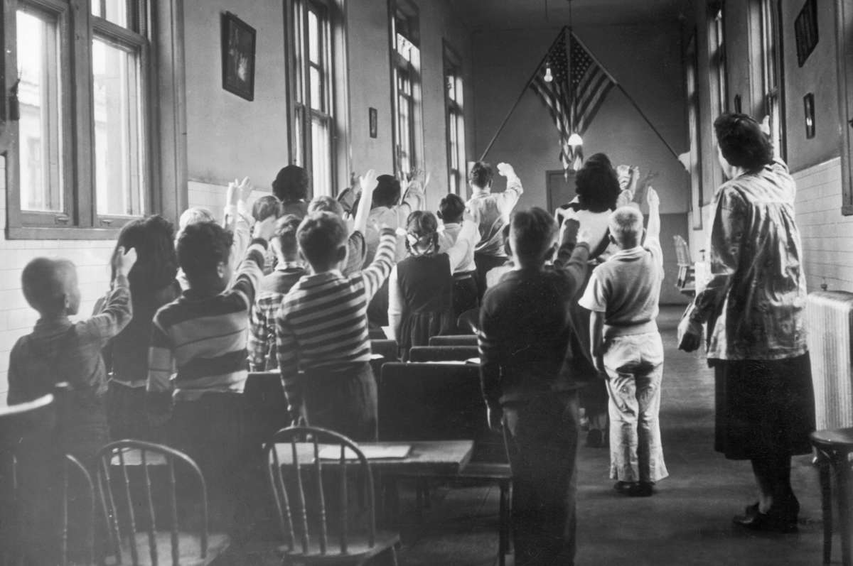 Children in a school at Ellis Island pledge allegiance to the U.S. flag, around 1940-1950.