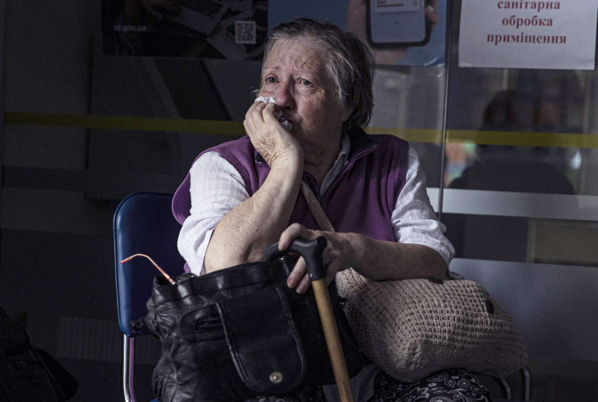 An elderly woman sits in a waiting area, her face conveying worry.