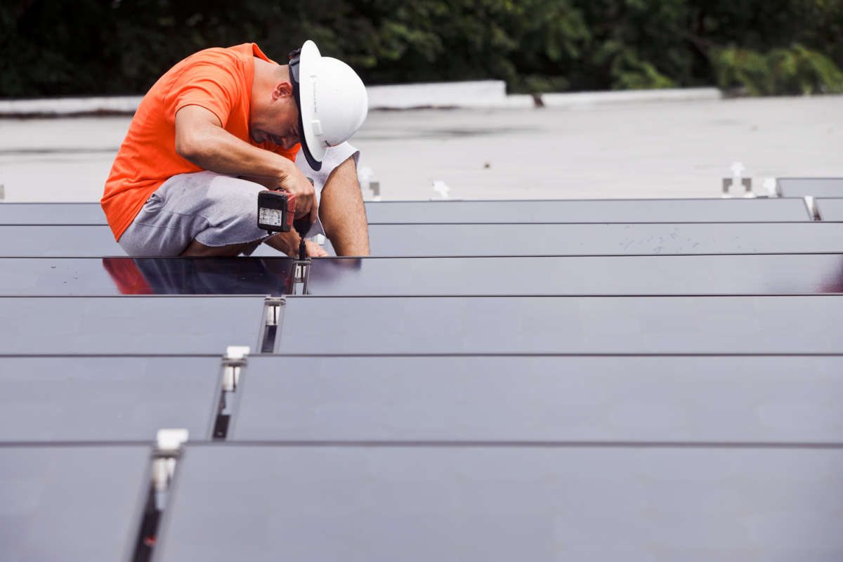 A worker installs solar panels on a rooftop