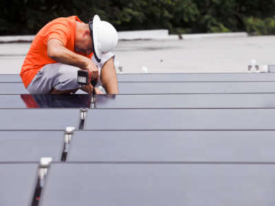 A worker installs solar panels on a rooftop