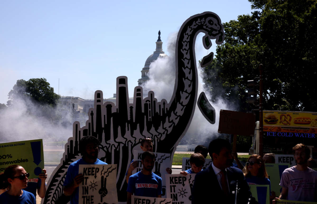 Activists simulate smoke coming from the back of a cardboard cut out of a dinosaur during an 'End Fossil Fuel' rally near the U.S. Capitol on June 29, 2021, in Washington, D.C.