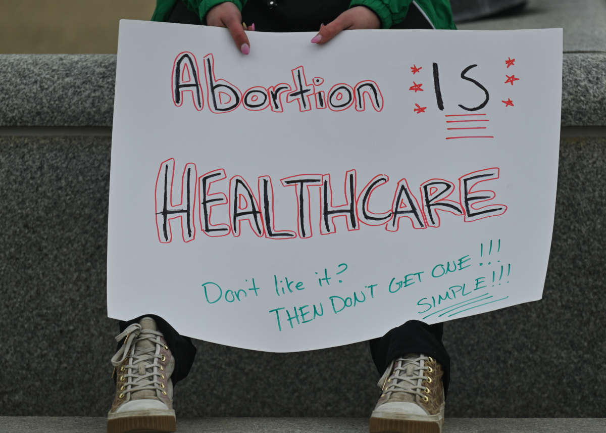 A protester hold a sign that reads, "Abortion IS HEALTHCARE. Don't Like it? THEN DON'T GET ONE!!! SIMPLE!!!"
