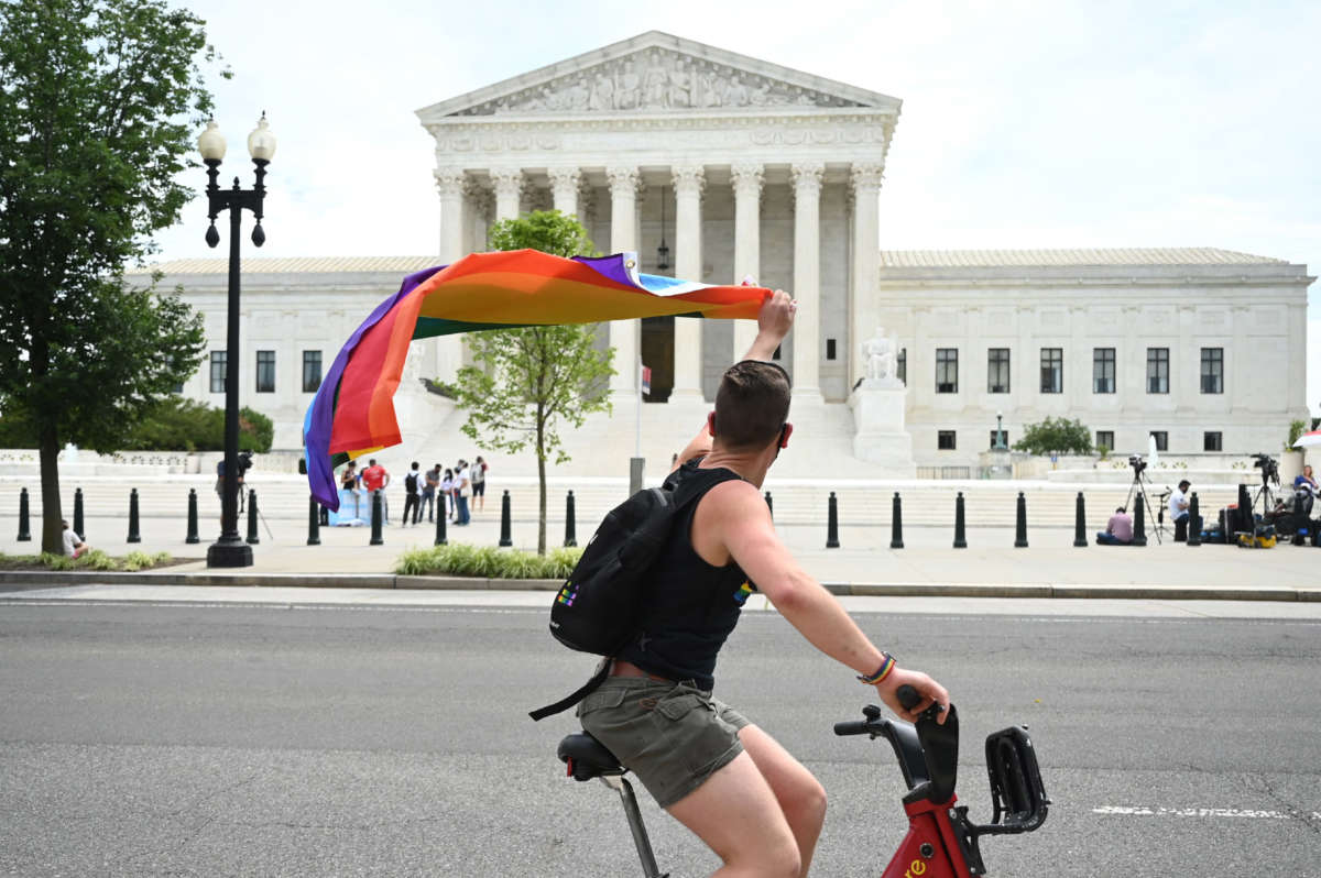 A man waves a rainbow flag as he rides by the U.S. Supreme Court on June 15, 2020, in Washington, D.C.
