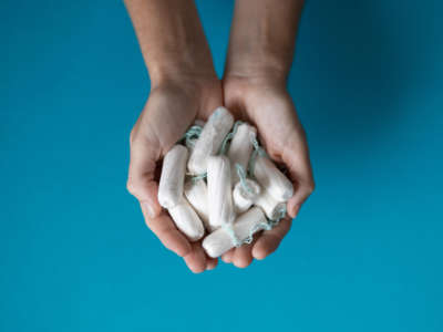 Hands hold several tampons in front of blue background