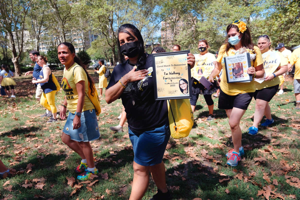 Masked marchers in matching yellow shirts carry photos of their loved ones that had passed away due to complications from covid