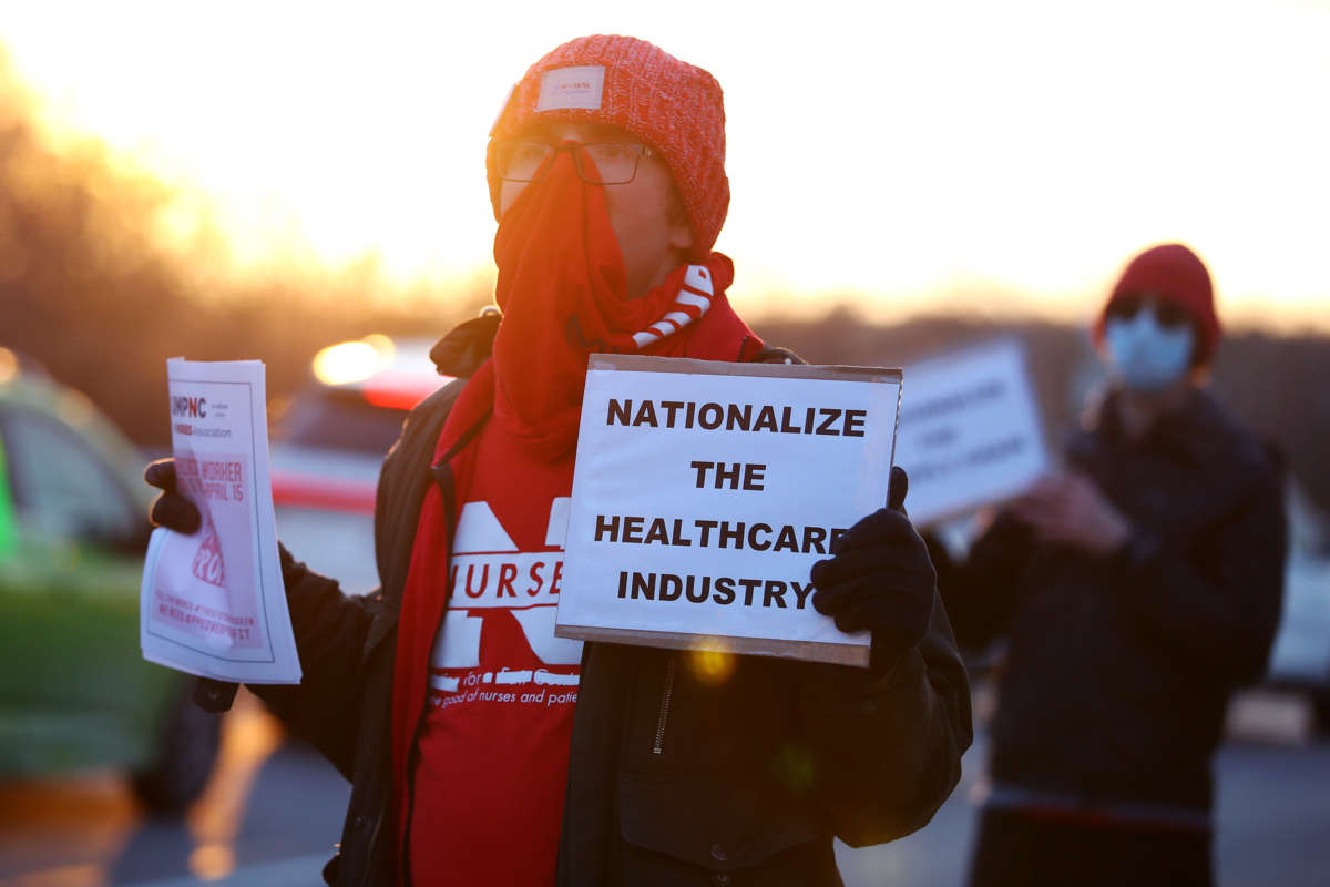 A backlit protester holds a sign reading "NATIONALIZE THE HEALTHCARE INDUSTRY" during an outdoor protest