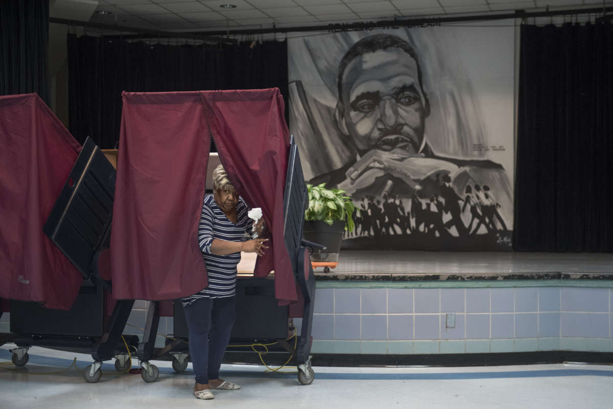 A Black woman leaves a voting booth next to a mural of Martin Luther King Jr.