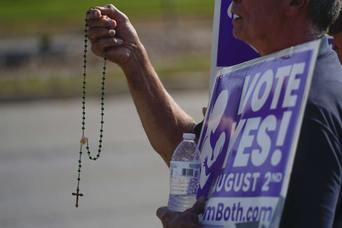 A person is holding up a rosarie while holding a sign in support of a measure voted on earlier this year in Kansas that would have removed abortion protections from the state constitution.