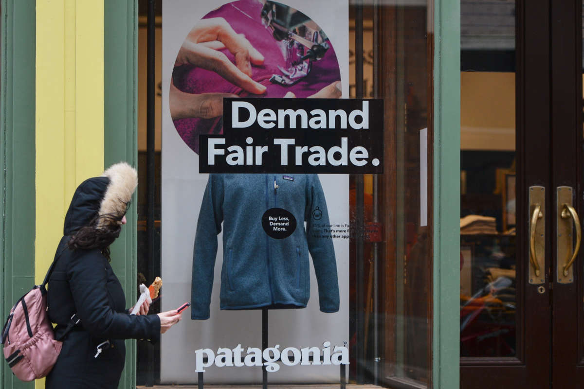 A sign on a Patagonia storefront window reads "Demand Fair Trade." as a person in a coat walks past it