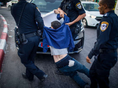 Uniformed police officers drag away a limp protester wearing a blue jacket and jeans