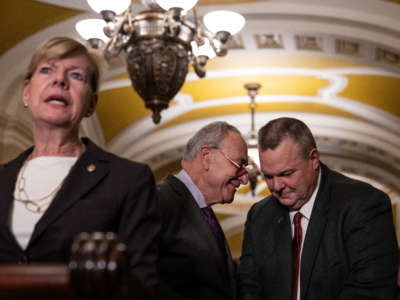 From left, Sen. Tammy Baldwin speaks to reporters as Senate Majority Leader Chuck Schumer confers with Sen. Jon Tester after meeting with Senate Democrats at the U.S. Capitol on November 29, 2022, in Washington, D.C.