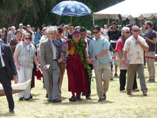 Closely protected and escorted by his interpreter (grey suit, left), the Dalai Lama wears a Hawaii leaf lei during a visit to Kualoa Park on Oahu. (Photo: Jon Letman)