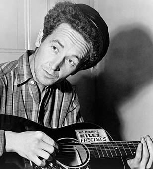 Woody Guthrie playing a guitar that has a sticker attached reading This Machine Kills Fascists, March 8, 1943.