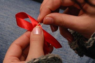 Hands hold an AIDS red ribbon pin