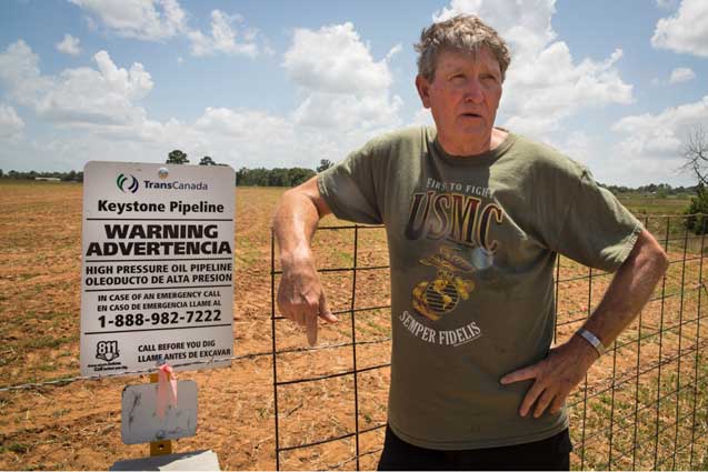 Michael Bishop next to a warning sign put up by TransCanda on his land. He points out the sign is incorrect which could be dangerous in the case of a spill for cleanup personal. The sign says oil pipeline when it is a bitumen pipeline. (Photo: ©2013 Julie Dermansky)