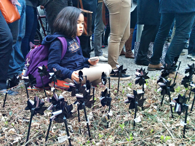 A child sits beside 111 black pinwheels, planted in the ground outside Chicago police headquarters. Activists arranged the display to show solidarity with protestors in Baltimore, where police have killed 111 people since 2010. (Photo: Kelly Hayes)