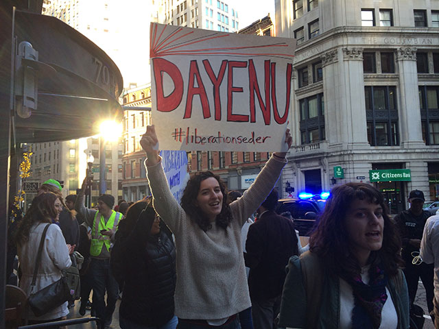 IfNotNow protester in Boston holds up a sign reading “Dayenu #LiberationSeder” while picketing outside of AIPAC. (Photo: Michelle Weiser)