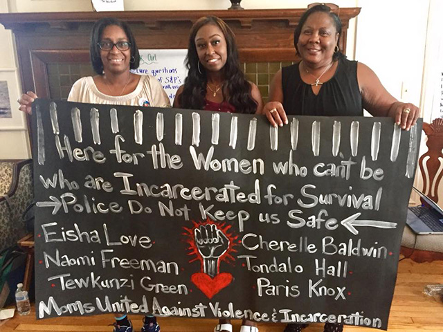 Cherelle Baldwin (center), mom Cynthia Long (left) and organizer Mary Shields from California Coalition of Women Prisoners (right) hold a banner prepared by Moms United Against Violence and Incarceration, which lists the names of criminalized survivors. (Photo: Holly Krig)