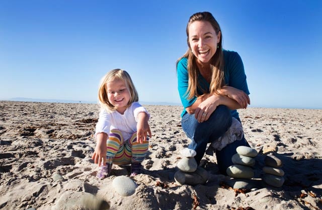 Hazel dismantles a stone tower on the beach as her mother, Rebecca Claassen, kneels next to her.