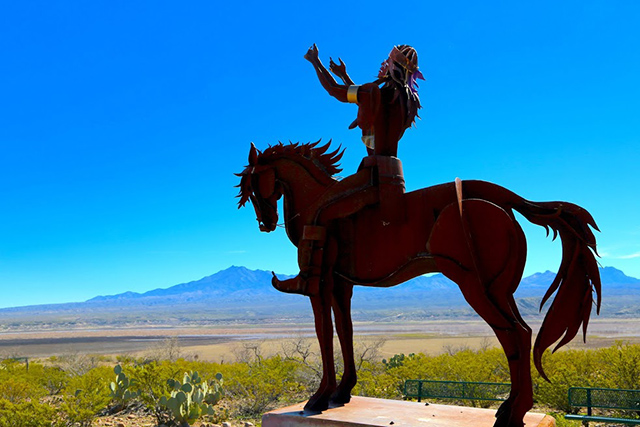 A statue of an Apache warrior reaching to the heavens stands at the memorial to Old San Carlos The valley beyond the statue is where Apache's endured as prisoners of war. (Photo: Roger Hill)
