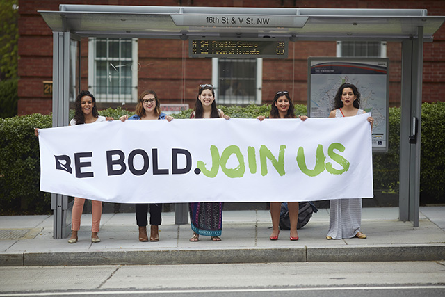 The “Be Bold” banner made on production day being held at a bus stop. (Photo: All* Above All)