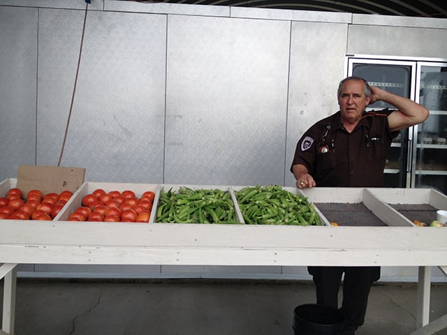 A police officer oversees incarcerated men selling vegetables at a produce stand down the road from the penal farm where Gonzalez was sent. Incarcerated men from the penal farm sell vegetables at the stand. (Photo: Dara Cooper)
