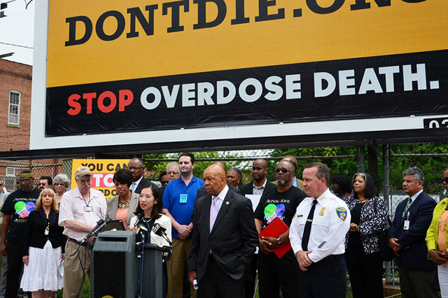 Baltimore Health Commissioner Leana Wen addresses a crowd in Baltimore in front of a billboard for DontDie.org, the website that links residents to the opioid overdose reversal drug naloxone.