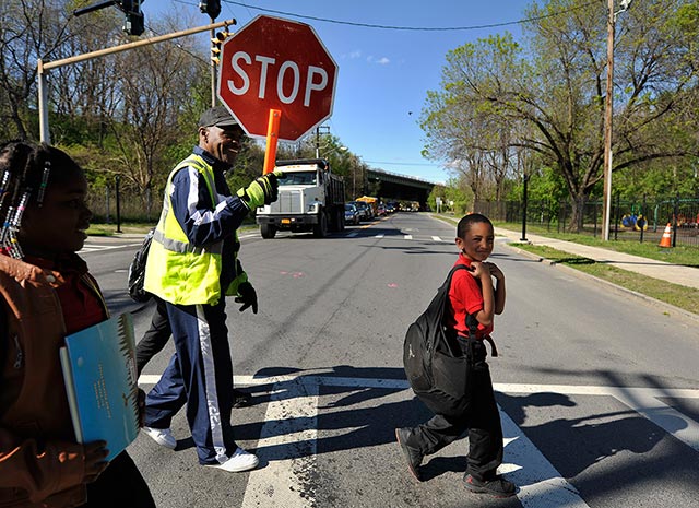 School crossing guard Be Be White stops traffic on South Pearl Street for children, including his son Brayton and Sanaiya, both six years old. (Photo: Earthjustice)