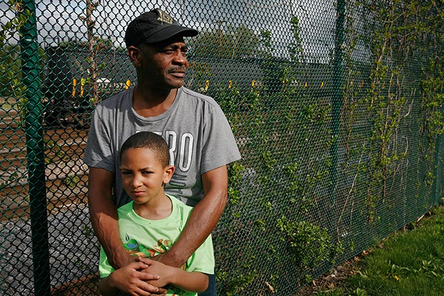 Be Be White and his son Brayton stand along the fence that separates the railroad tracks from Ezra Prentice Homes. (Photo: Earthjustice)
