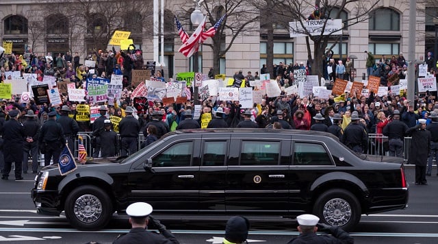 The presidential motorcade drives by as protesters line the streets during the 58th Inauguration in Washington, DC, on January 20, 2017.