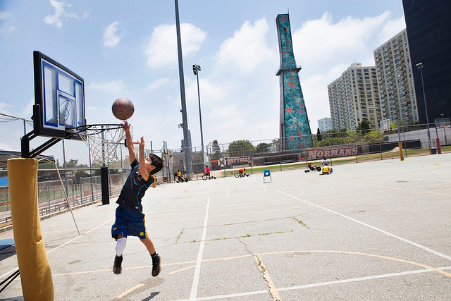 A boy plays basketball in front of an oil well that is covered with large colorful flowers and is located next to Beverly Hills High School. Wells like this are hidden throughout Los Angeles. (Photo: Sarah Craig / Faces of Fracking)