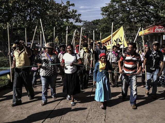 V&aacute;squez, center, leads march to Presidential Palace to demand a just trial for Berta C&aacute;ceres' assassination, Tegucigalpa. The poles, representing authority, are used by Lenca elders. (Photo: Beverly Bell) 