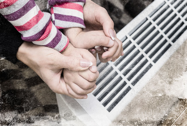 Mother and child warming hands by heater. (Photo: Yevhen Prozhyrko / Shutterstock)